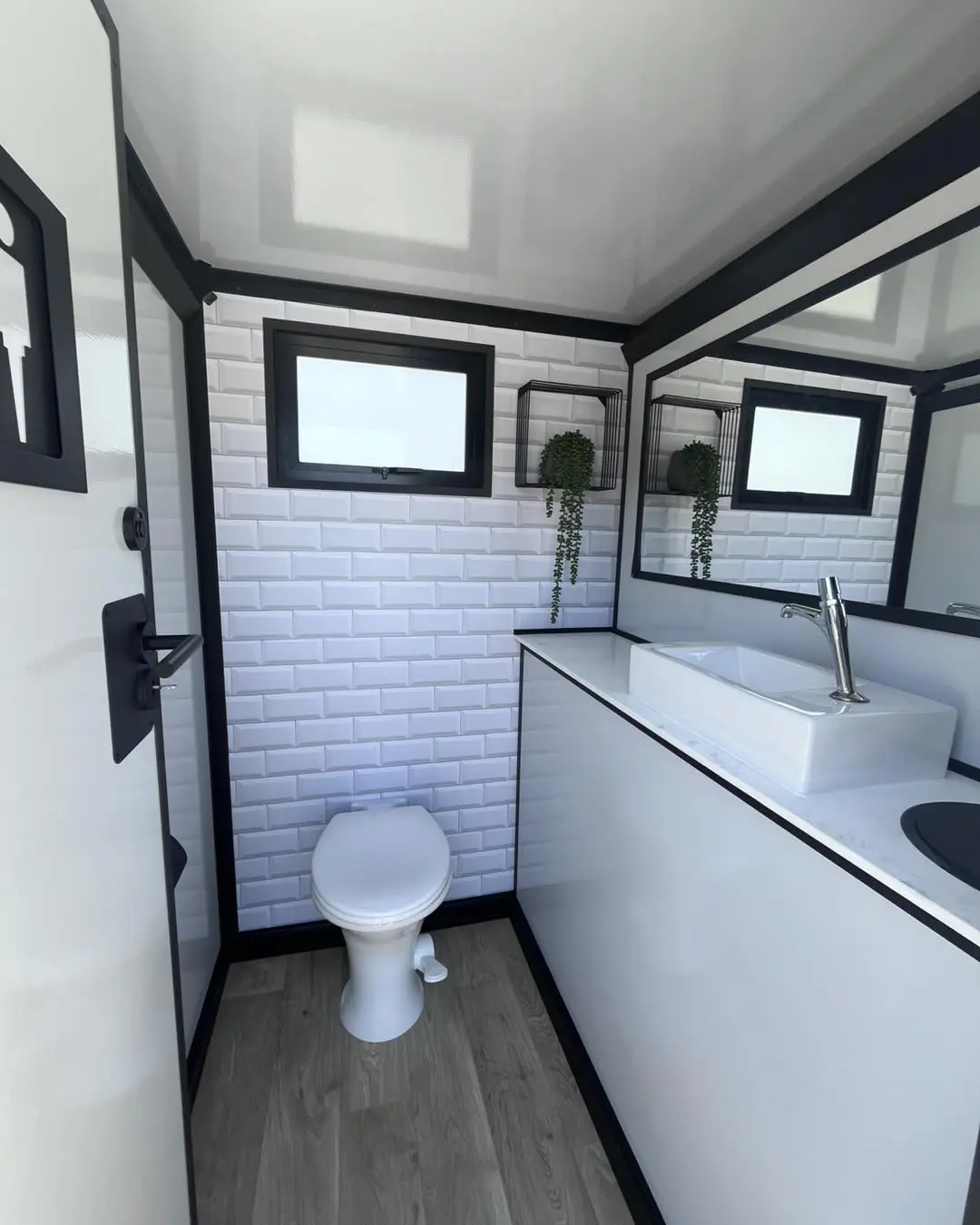 Inside a restroom trailer stall with a flushing toilet, vanity and mirror