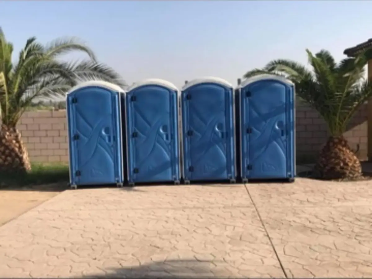 Row of four blue porta potties set out near palm trees for an outdoor event