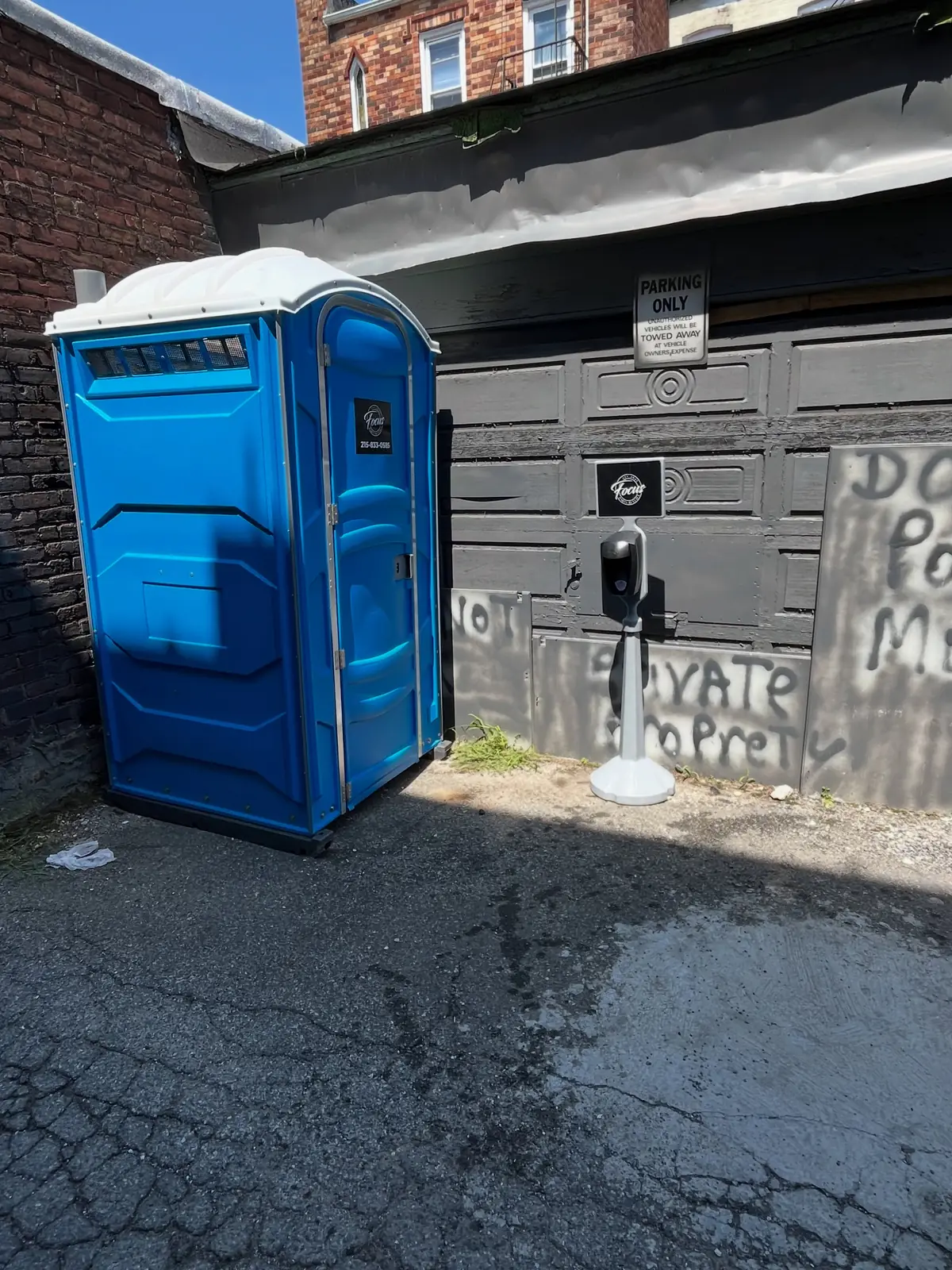 One blue porta potty placed beside a building wall on an asphalt jobsite