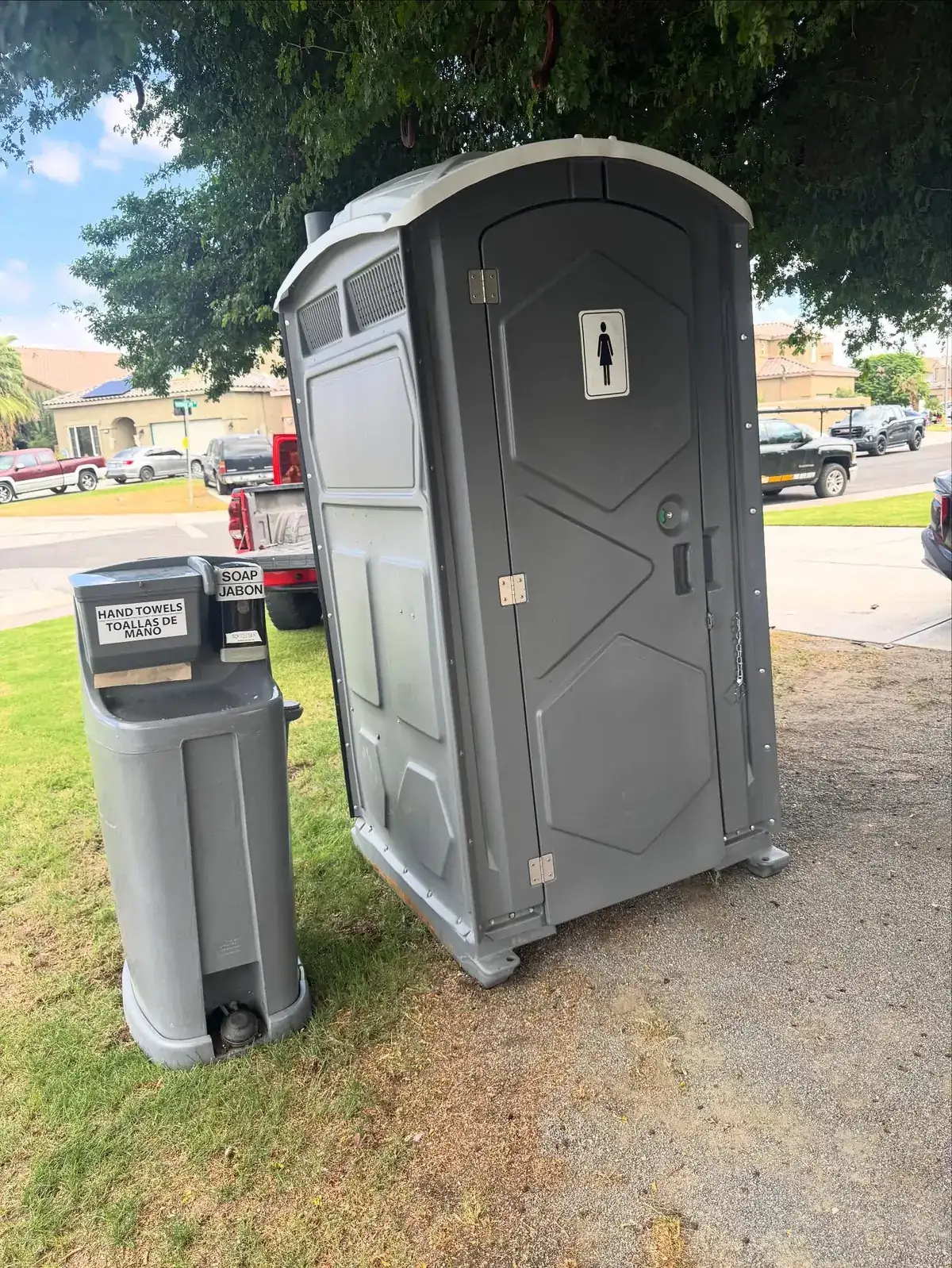 A standard porta potty and a hand wash station placed on level grass