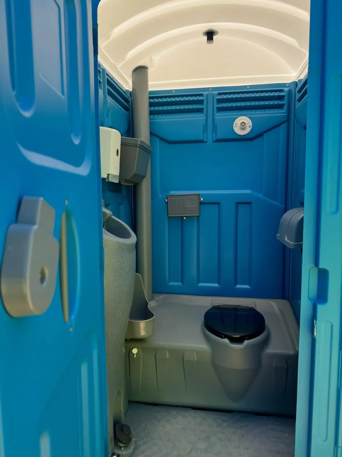 Inside a standard porta potty with the toilet seat, urinal and paper holder