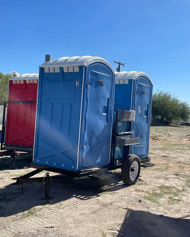A standard porta potty mounted on a small towable trailer at a work site