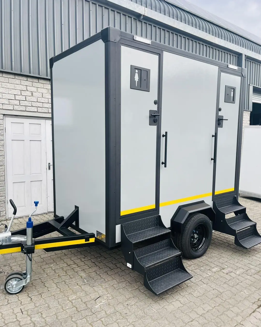 Gray and white two-stall restroom trailer parked on level ground